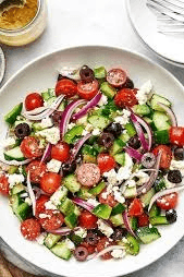 GREEK SALAD No-lettuce mix of fresh, chunky vegetables, featuring tomatoes, cucumbers, green bell peppers, red onion, Kalamata olives, and feta cheese. Key dressings include extra virgin olive oil, red wine vinegar, and dried oregano.